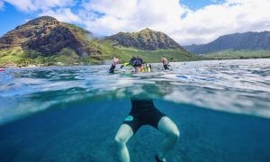 A man wearing snorkel gear, floating and posing for a picture, with a backdrop of mountains